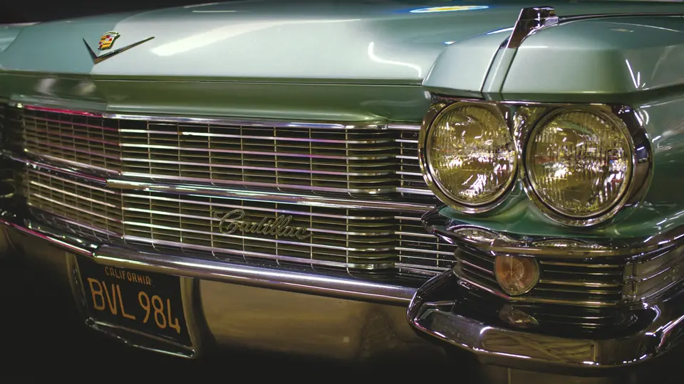 Close up shot of the grill and front driver side headlight of an old caddilac with a blue-ish gray finish.