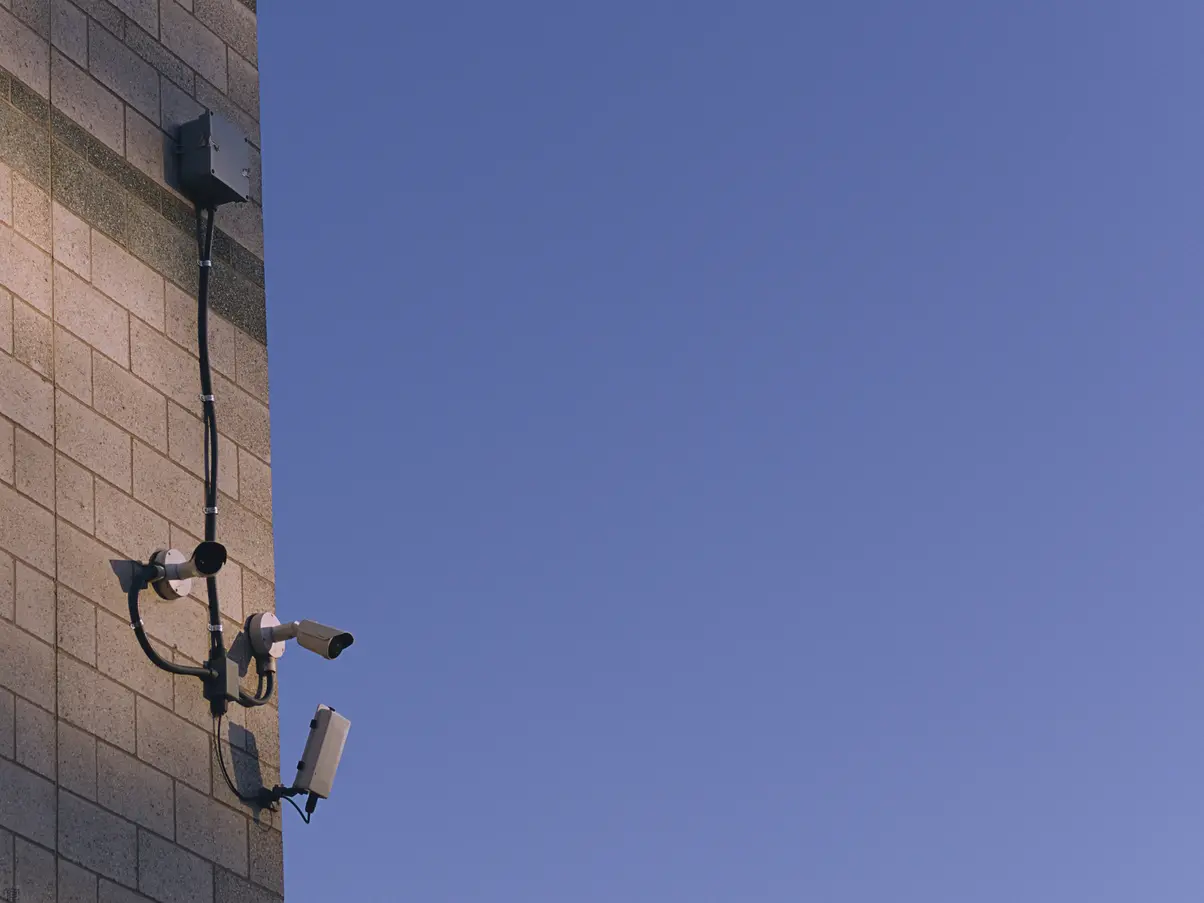 Two security cameras installed on the corner side of a building pointing in two different directions with a junction box wired up above them.