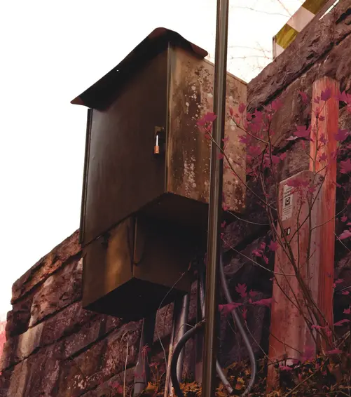 An electric box sites on the side of a rural bridge with a padlock on the latch.