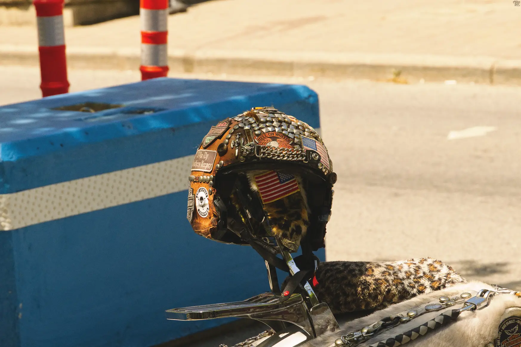 A leather biker helemet sits on the back sissy bar covered in various patches and studs.