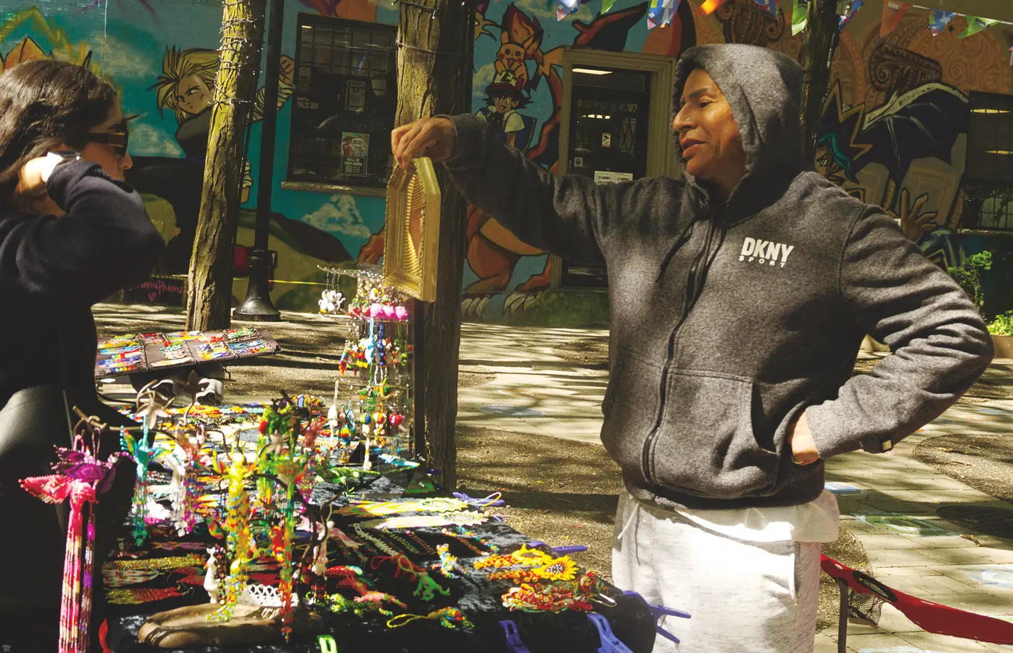 A street vendor holds up a small mirror so a customer can see the beadwork as they try it on.