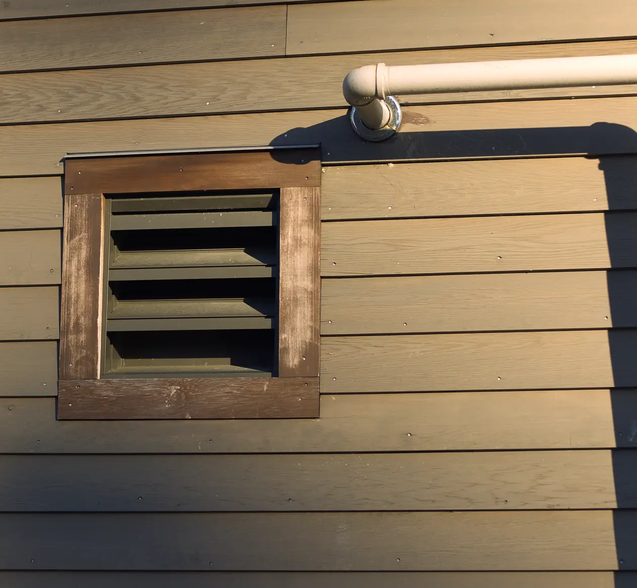 Square vent made out of wood on the side of a building being lit by the sun.