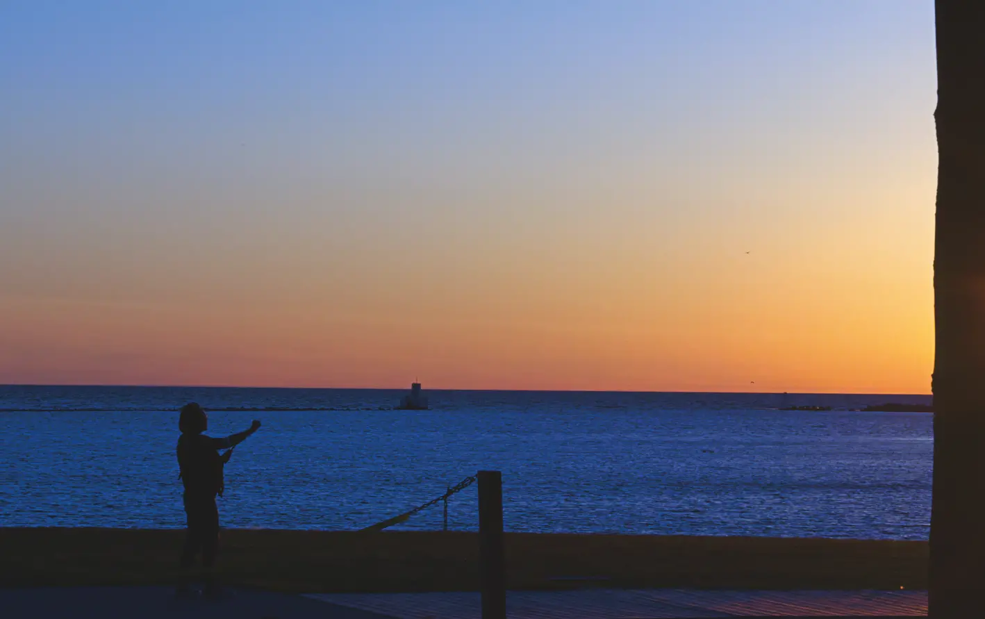 A woman holds up her phone to take pictures of the sunset over the lake.