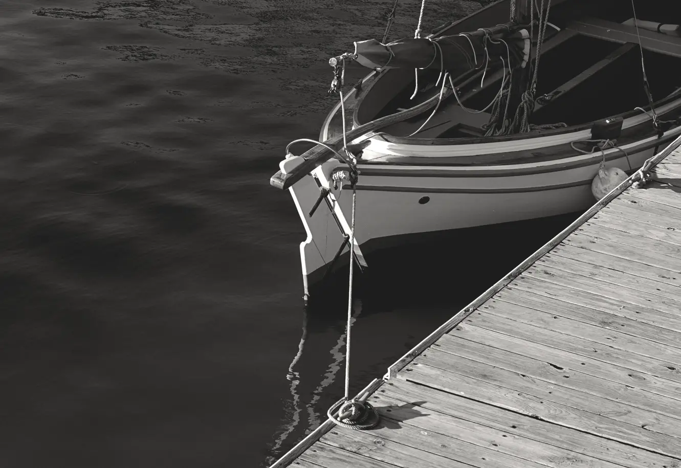 Black and white photo of a small personal sail boat docked on a pier.