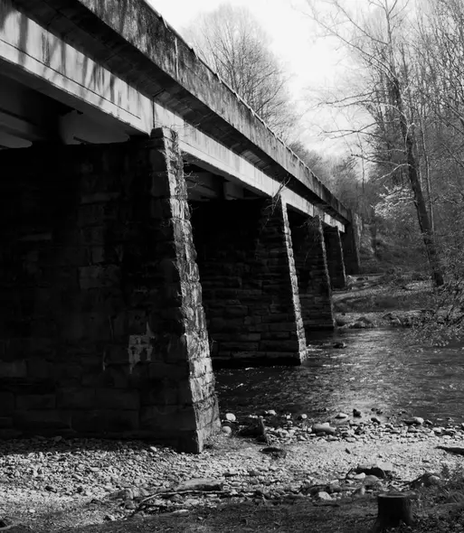 Underside of a rock pillar bridge in the middle of a nature trail that crosses a small river.